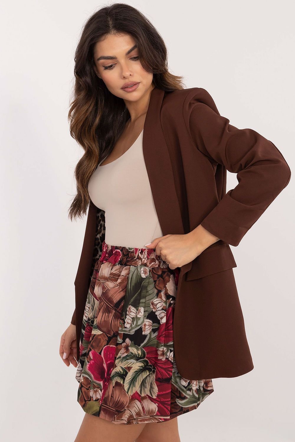 Een vrouw draagt een stijlvolle minirok met bomber snit en bloemenprint, perfect voor een casual zomerlook, beige t-shirt met een bruine blazer, beige achtergrond,