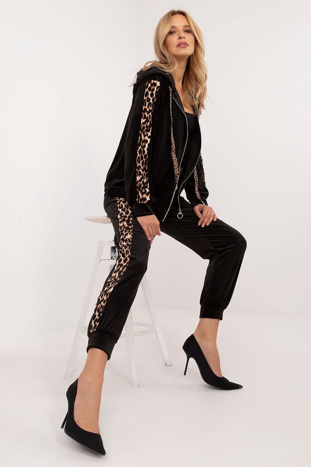 Een vrouw draagt met een velours damesset met sweatshirt en broek, comfortabel en stijlvol met dierenprintdetails, perfect voor alledaags gebruik,zittend