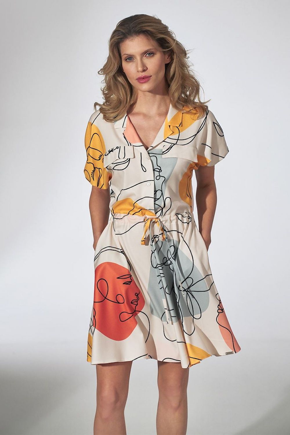 Vrouw met halflang golvend haar draagt Vrouw met halflang golvend haar draagt een zomerse dagjurk met korte mouwen, een abstracte gezichtenprint in pastelkleuren en een strikceintuur in de taille. een abstracte gezichtenprint in pastelkleuren en een strikceintuur in de taille