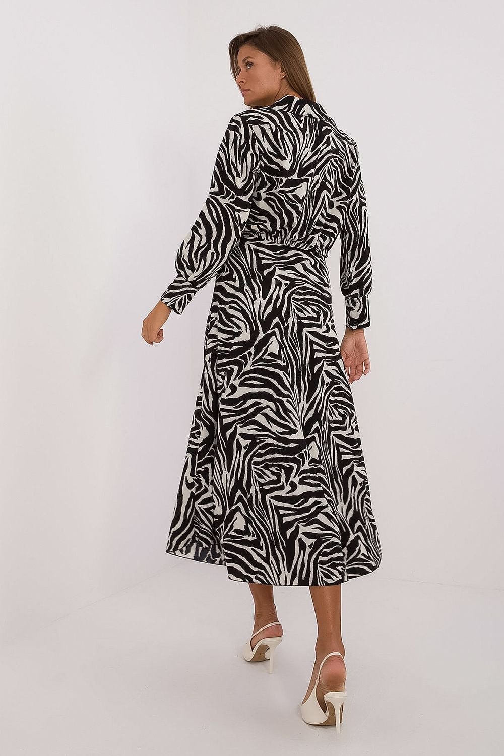 Een vrouw draagt een elegante, zwart-witte jurk met een opvallend zebrapatroon en een wikkelmodel bovenstuk met lange mouwen,van achter kant