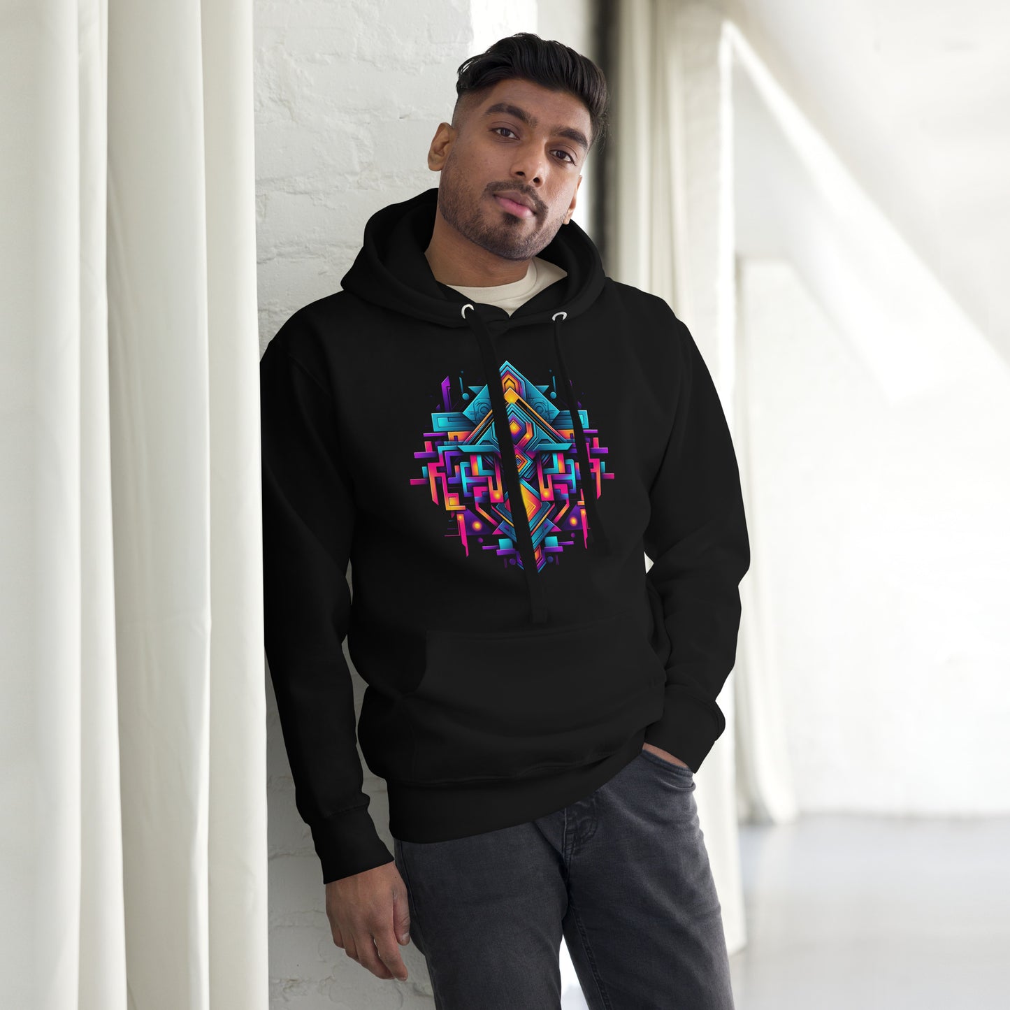Een zwart unisex premium hoodie met een geometrische afbeelding, gedragen door een man, vooraanzicht, met een gordijn als achtergrond
