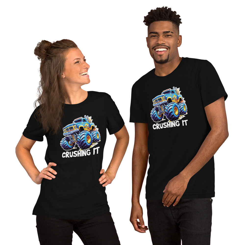 Een zwart unisex T-shirt met een afbeelding van een monstertruck, vooruit kijkend, met een lachende man en vrouw, op een witte achtergrond.