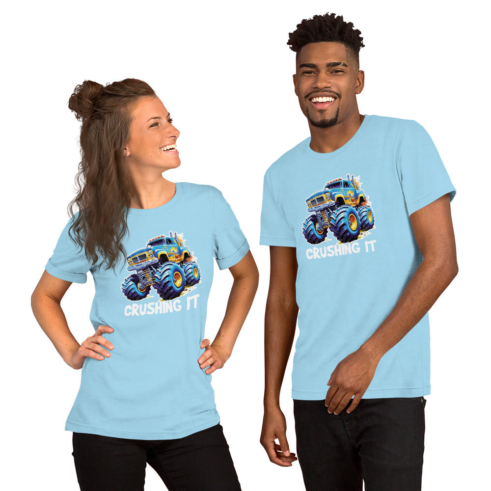 Een ocean blue unisex T-shirt met een afbeelding van een monstertruck, met een lachende man die vooruit kijkt en een lachende vrouw die ook recht vooruit kijkt, tegen een witte achtergrond.