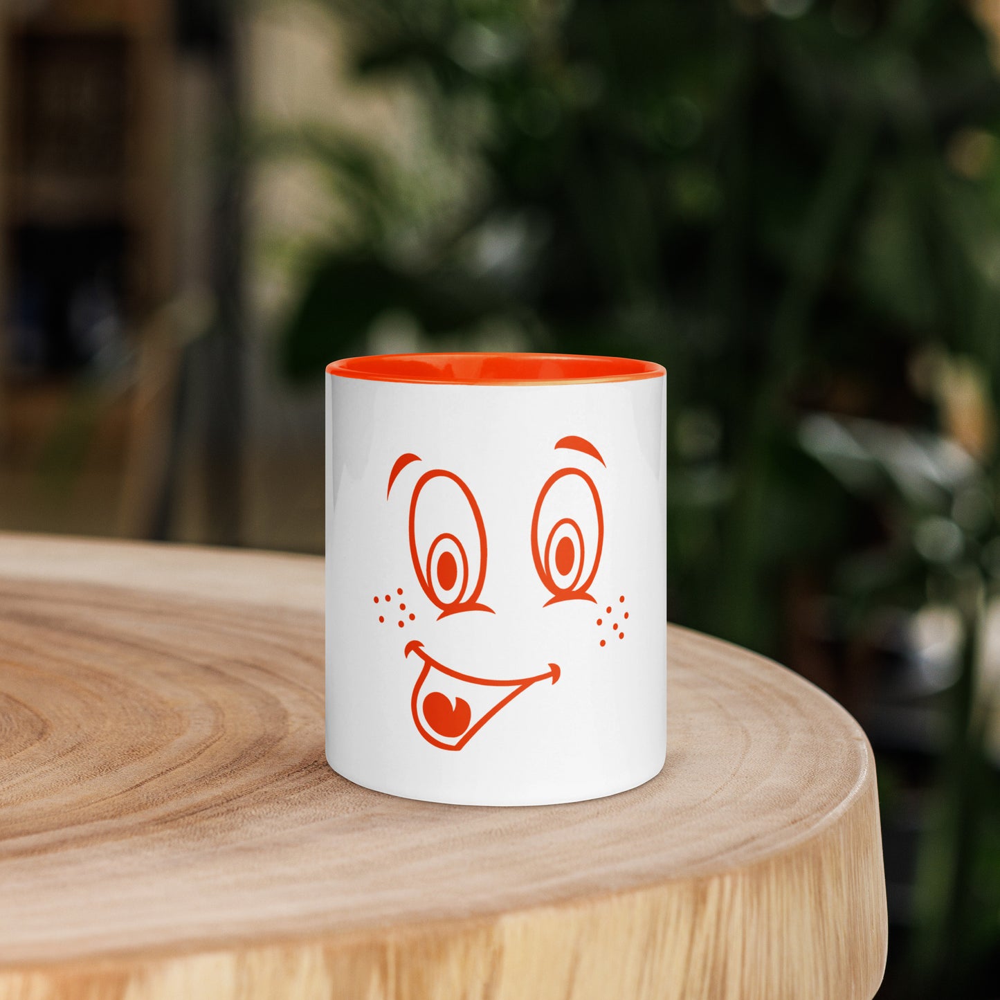 Een witte keramieken mok met een vrolijke cartoonafbeelding, De binnenkant van de mok is oranje. Het betreft een vooraanzicht van een mok van 11 oz, met de afbeelding aan de voorkant sta op een houten ronde tafel