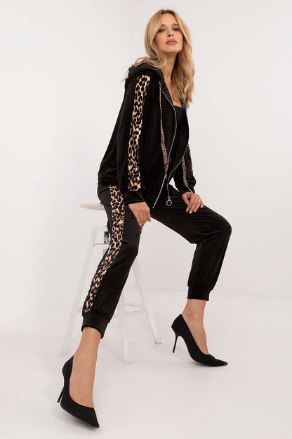 Een vrouw draagt met een velours damesset met sweatshirt en broek, comfortabel en stijlvol met dierenprintdetails, perfect voor alledaags gebruik,zittend