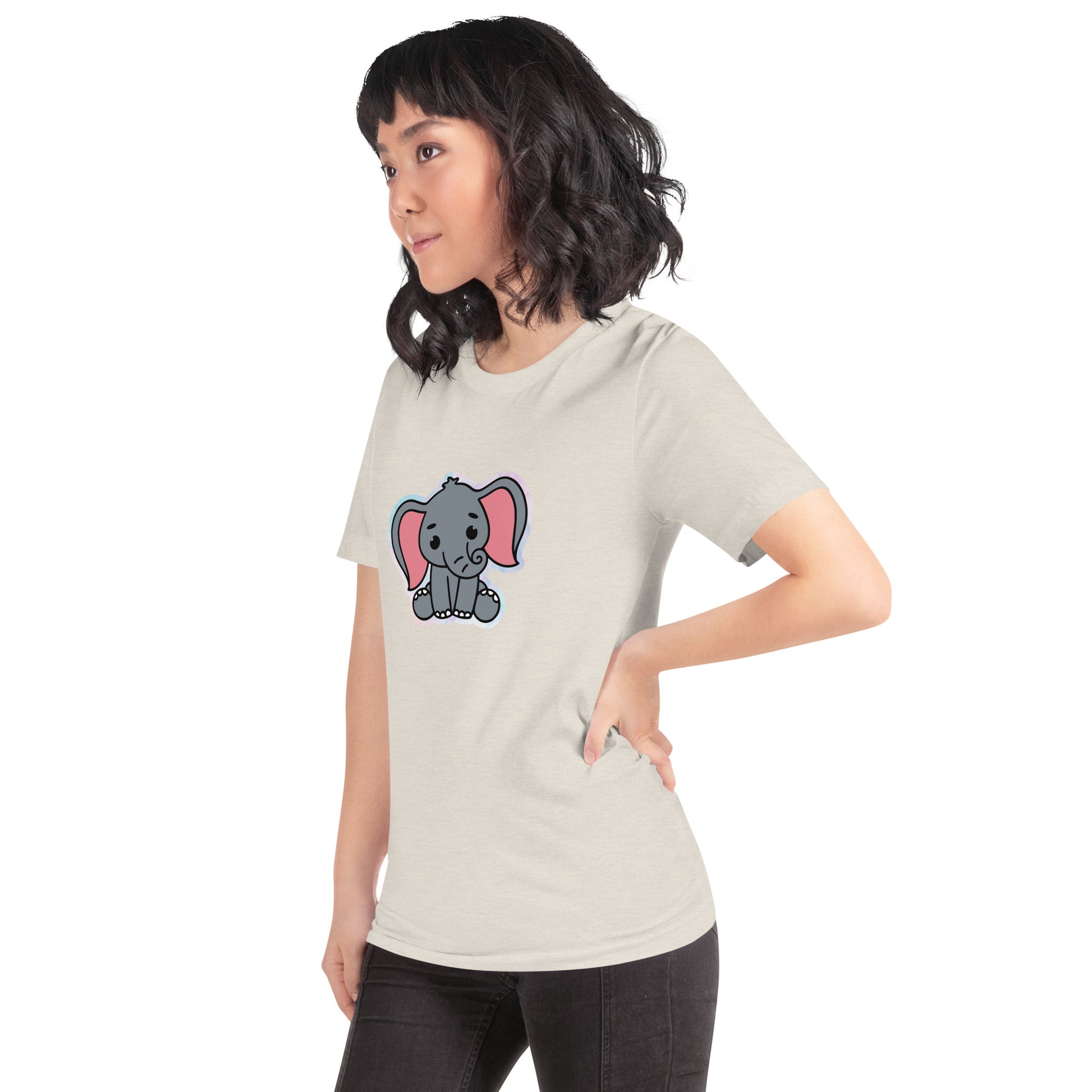 Een heather dust unisex T-shirt met een afbeelding van een grappige grijze baby olifant, gedragen door een vrouw, aan de linksvoort op een witte achtergrond.